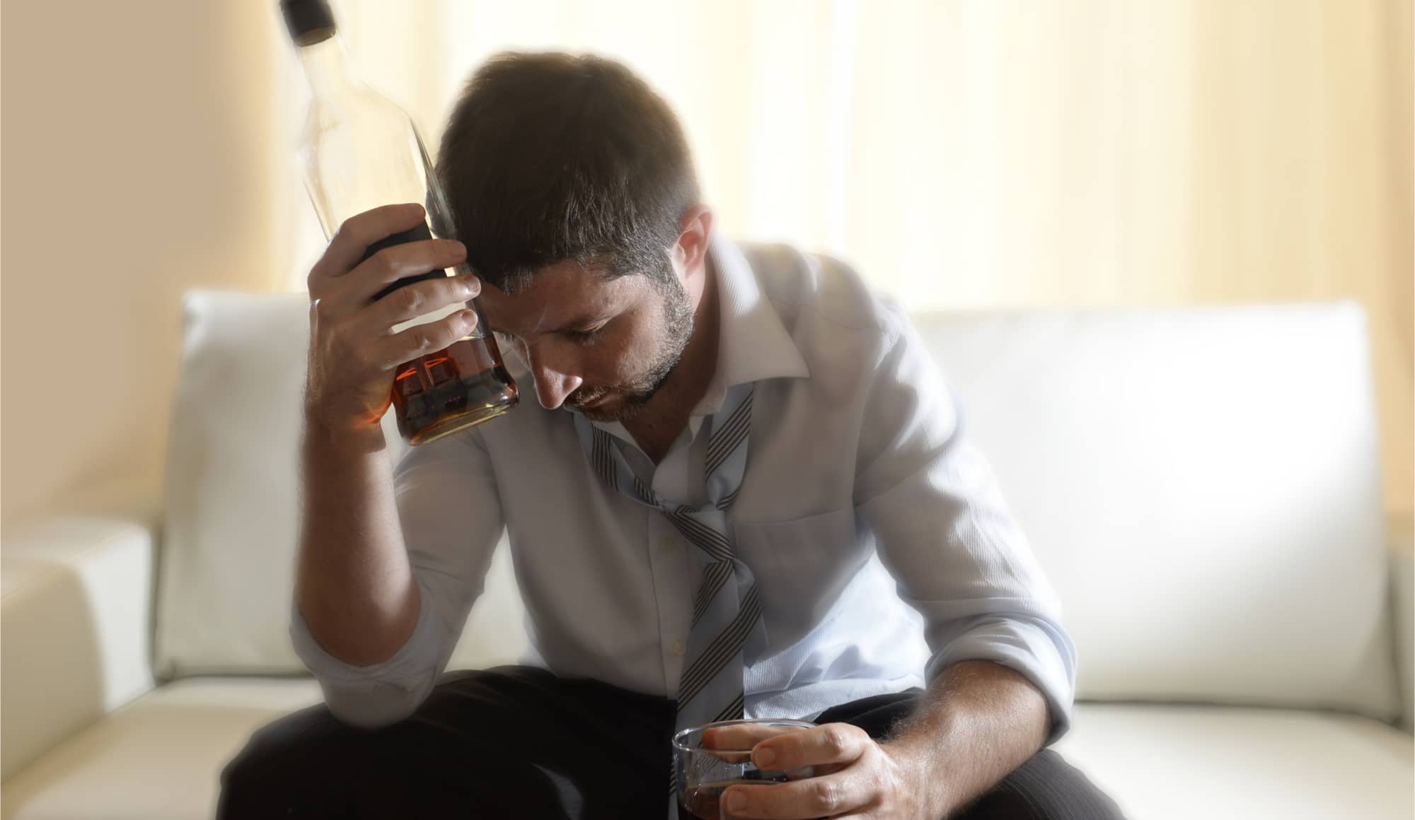 Celebrities and Alcohol Addiction Pathfinders - A man sits in his couch and has drink after drink to deal with his anxiety.