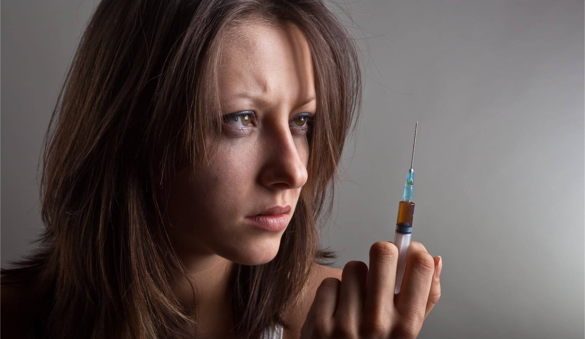 Heroin Addiction What to Watch For Pathfinders - A woman stares at a needle with heroin in it. If you think a loved one is addicted to heroin you need to how to tell if someone is on heroin by looking for the signs here.