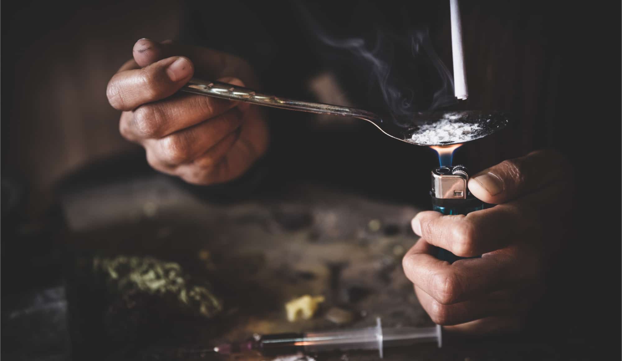 How to ask for help with drugs Pathfinders - Photo of a mans hands as he holds a lighter under a spoon with white powder in it as he sucks the smoke through a straw.
