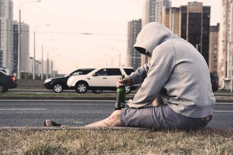 How to Tell if Someone is Drunk - A man sits in the curb and drinks a large beer. If you know someone who struggles with alcohol learn how to tell if someone is drunk and get help for them at an alcohol rehab.