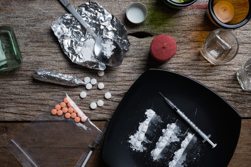 Most Addictive Drugs - Photo looking down on a table with an assortment of the most addictive drugs including Pills, Heroin, Cocaine and Alcohol.