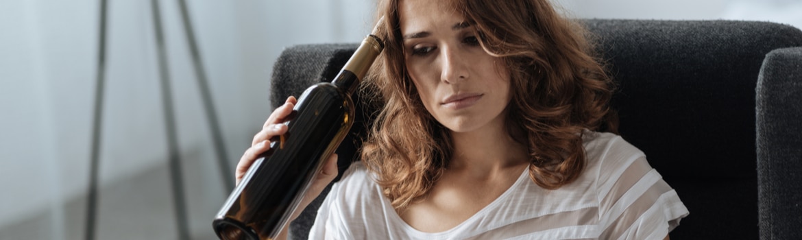 Partial Hospitalization Program (PHP) in Arizona Pathfinders - A woman is experiencing depression and is drinking a bottle of wine to try and cope with her mental health disorder, while contemplating her treatment options, such as partial hospitalization programs in Arizona to help treat her substance abuse and mental health disorder.