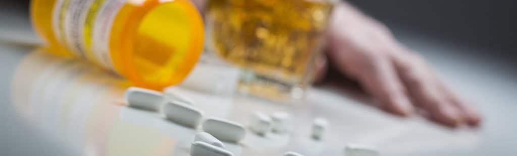 Benzodiazepine Addiction - Mixing alcohol with a benzodiazepine addiction can lead to very serious problems including death. This is a photo of a woman passed out with a bottle of Xanax and a glass of alcohol out of focus next to her.